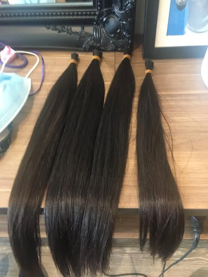 Four thick ponytails of cut dark hair bound with gold elastics on a timber bench