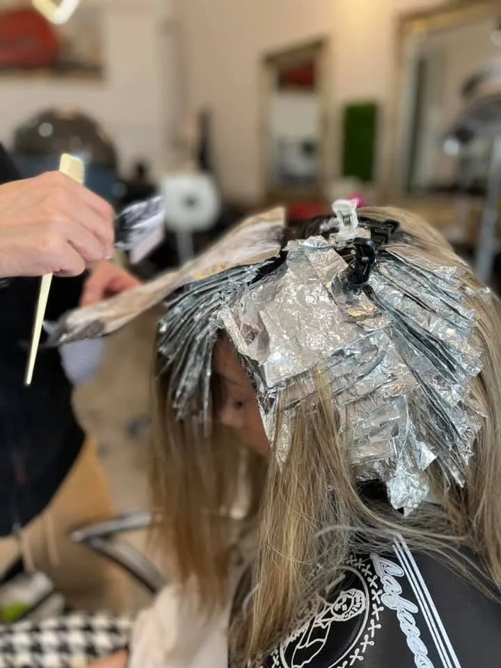 Stylist drawing tint brush through a foiled section — blonde client, salon floor behind