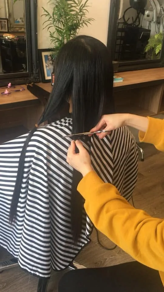 A stylist mid-cut at H.A.T Hair — scissors in hand, gilt-framed mirror and potted palm behind, Greville Street daylight