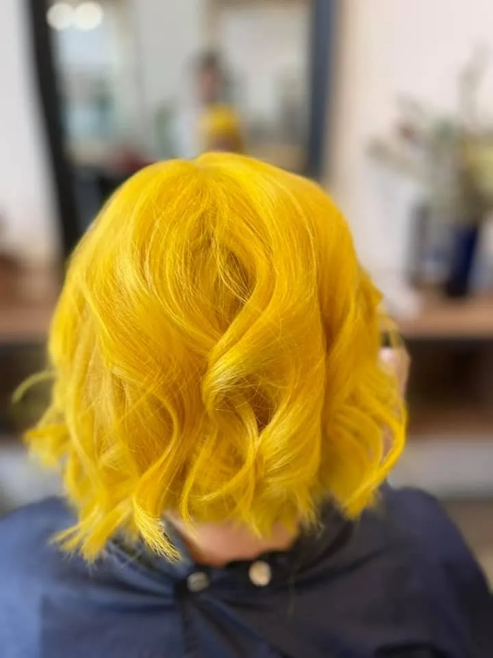 Yellow bob back view — mirror reflection, bottles on shelf, navy cape