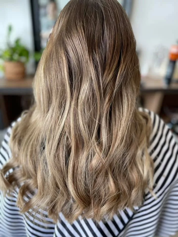 Bronde balayage waves over a striped top — potted plant and timber shelving behind